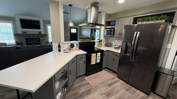 A modern kitchen with grey cabinets, a stainless steel refrigerator, a microwave, and a large island with a sink. - Charming 3-bedroom house with fitness room and AC in Bandera (Bandera)