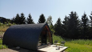 A small, modern cabin with a sloped roof, a wooden deck, and a glass door leading inside.