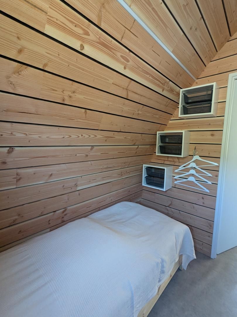 Una habitación pequeña y acogedora con paredes de madera, una cama individual y espacios de almacenamiento integrados.