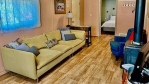 A cozy room with a sofa, a small table, a blue chair, a heater, and a bed in the background.