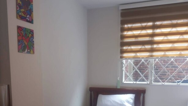 A small, simple room with a bed, a desk, and a chair. There are two windows with blinds, and the walls are plain. - Room-cozy Guest Room in Bogotá's Heart (Bogotá)