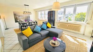 A modern living room with a grey sectional sofa, a round black coffee table, and a dining area with a black table and chairs. - Chic Urban Stay 2BR with parking (Luxembourg City)