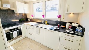 A modern kitchen with white cabinets, a black countertop, and a window with a view of houses. - Chic Urban Stay 2BR with parking (Luxembourg City)