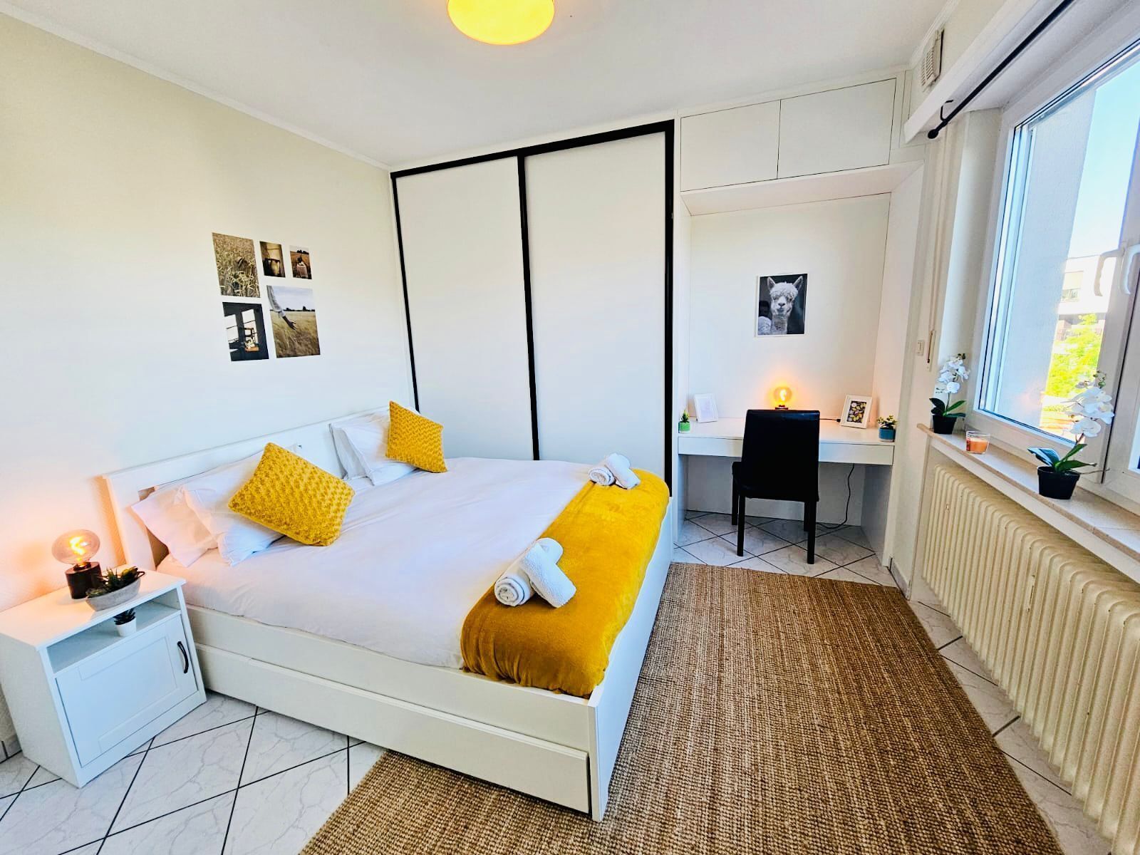 Un dormitorio moderno con cama, mesita de noche, escritorio, silla y vistas al exterior.
