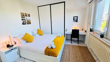 Un dormitorio moderno con cama, mesita de noche, escritorio, silla y vistas al exterior.