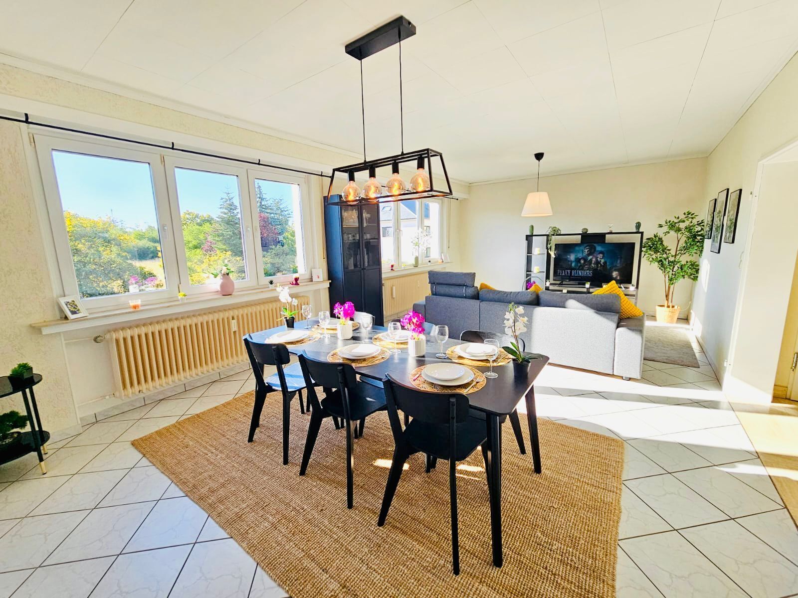 A modern dining area with a table set for four, a black cabinet, and a television in the background.