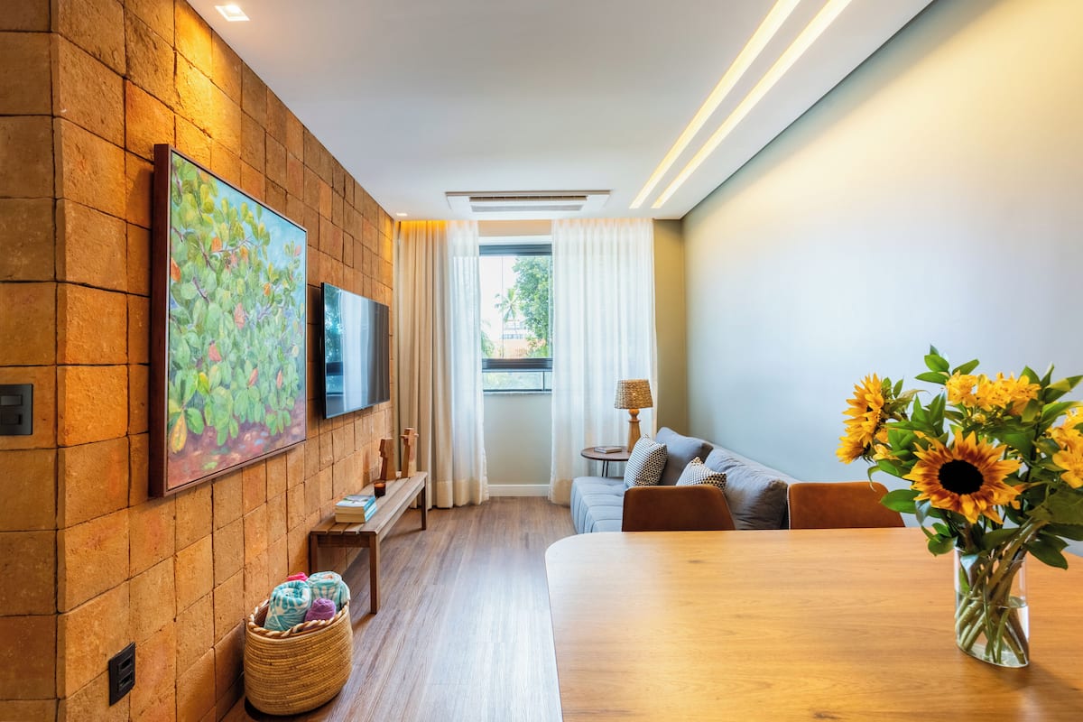 A modern living room with a wooden floor, a sofa, a dining table, and a TV mounted on the wall.