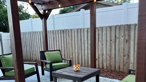 Une terrasse extérieure agrémentée d’une pergola en bois, d’une table avec des chaises et d’un tapis décoratif.
