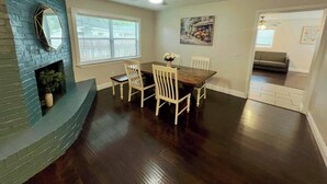 Un coin repas avec une table en bois foncé, des chaises blanches, une cheminée et un ventilateur de plafond.