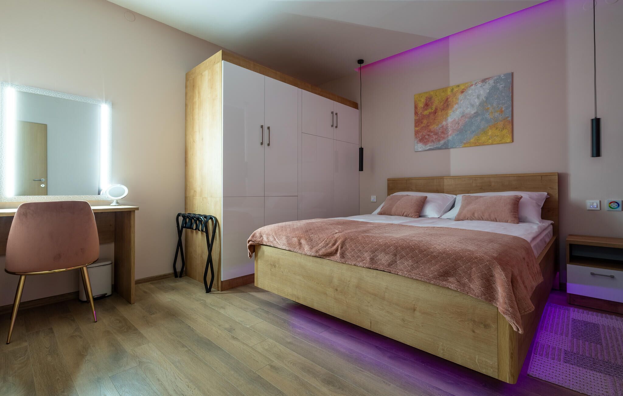 A bedroom with a wooden bed, a desk with a chair, a wardrobe, and a painting on the wall.