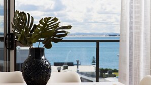 A room with a view of the sea, a black vase with a plant, and a white sofa.