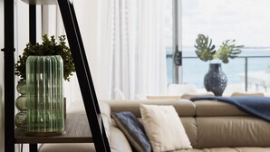 A modern living room with a sofa, a glass vase with plants, and a view of the sea through large windows.