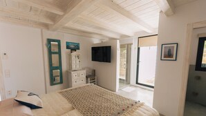 A bedroom with a bed, a TV, a dresser, and a door leading to an outdoor area.