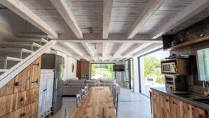 A modern kitchen with wooden cabinets, a long dining table, and built-in appliances.