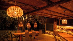 An outdoor dining area with a wooden table and chairs, surrounded by a stone wall and trees.