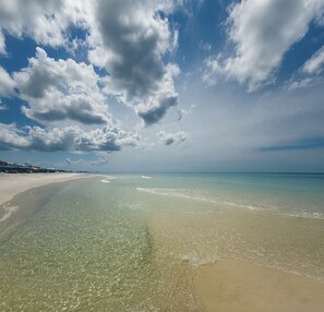 A beach with clear water, a sandy shore, and a partly cloudy sky.