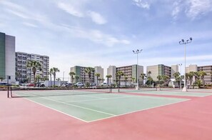 Ein Tennisplatz im Freien mit umliegenden Gebäuden und Palmen.