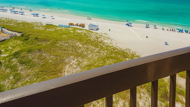 A beach with clear turquoise water, a sandy shore, and a wooden balcony railing. - The Emerald Edge - Pinnacle Port (Panama City Beach)
