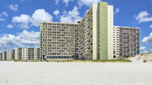A multi-story hotel with a flat facade and balconies, located on a sandy beach with a clear sky. - The Emerald Edge - Pinnacle Port (Panama City Beach)