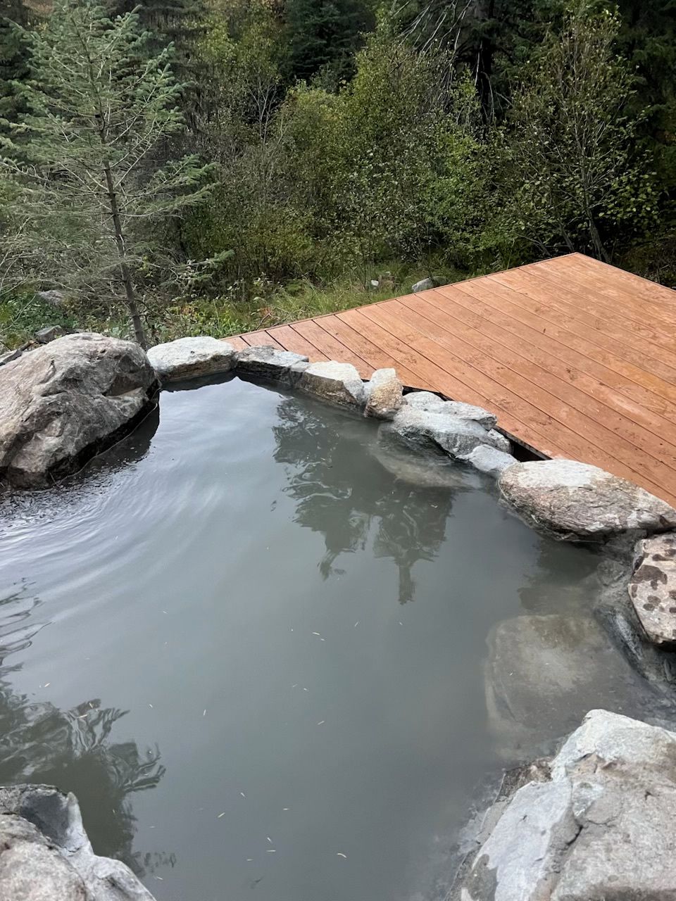 A wooden deck surrounding a small pond with rocks forming a natural edge.