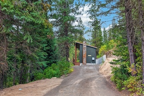 A forested path leading to a modern building with a metal door and a small porch.