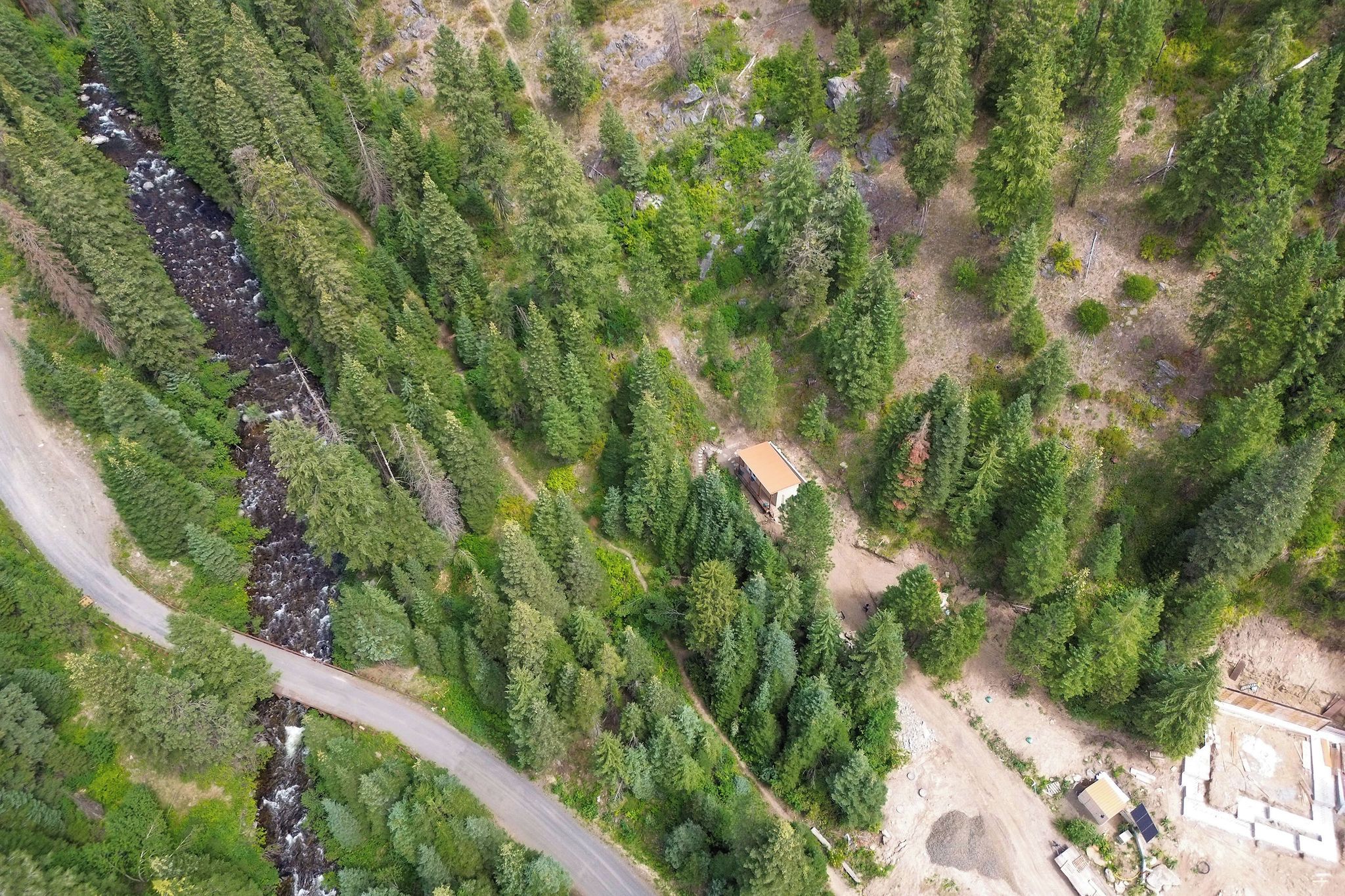 Vue aérienne d’une zone boisée, avec une route sinueuse, un petit bâtiment et un chantier de construction.