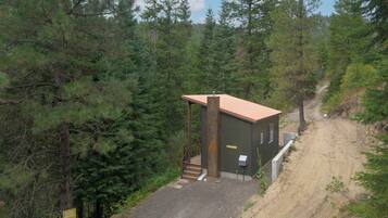 A small cabin with a red roof, surrounded by dense forest, accessible by a gravel path.