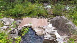 A wooden bridge over a small stream surrounded by rocks and greenery. - Private Hot Spring | River | Brundage | Off Grid (New Meadows)