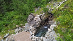 A wooden deck overlooking a natural hot spring with a stone wall and rocks. - Private Hot Spring | River | Brundage | Off Grid (New Meadows)