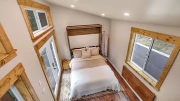 A bedroom with a wooden headboard, a large bed with white bedding, and a window with a wooden frame.