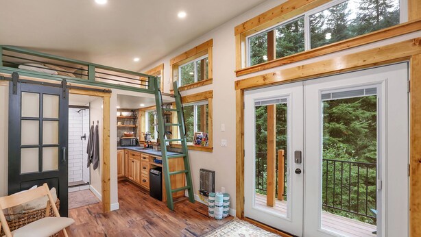 A spacious kitchen with wooden cabinets, a loft area, and large windows offering a view of the outdoors. - Private Hot Spring | River | Brundage | Off Grid (New Meadows)