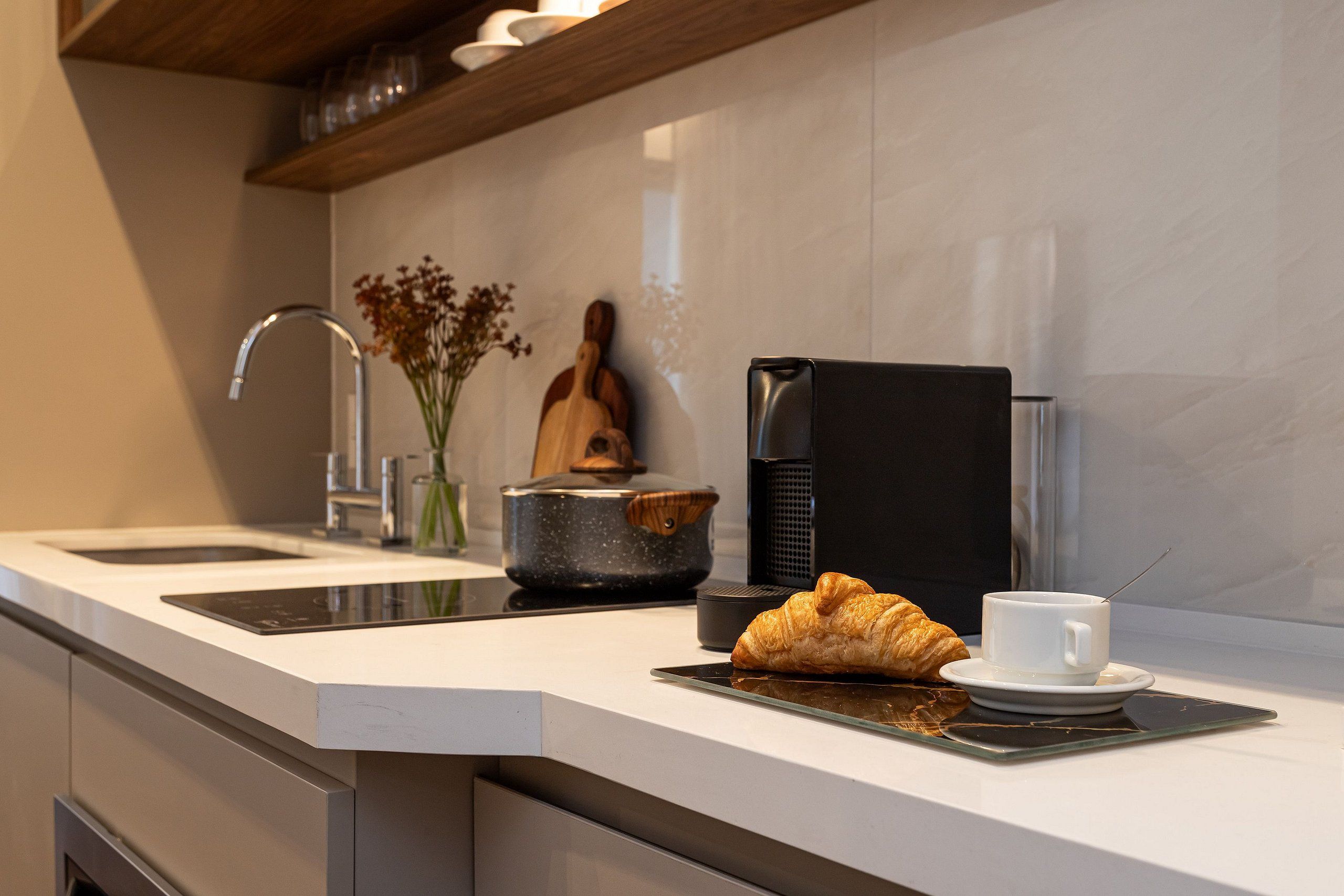 A modern kitchen with a coffee maker, a croissant, and a cup on the counter.