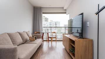 Uma sala de estar moderna com sofá, TV, armário de madeira e varanda com vista para a cidade.