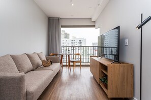 A modern living room with a sofa, TV, wooden cabinet, and a balcony with a city view. - Apartamentos mobiliados com excelente vista e localização - Higienópolis (São Paulo)