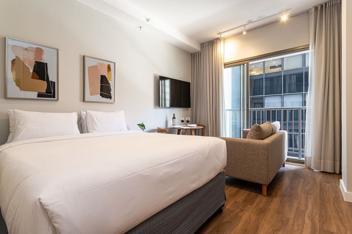 Une chambre d’hôtel dotée d’un grand lit, d’un coin salon, d’une télévision à écran plat et d’une grande fenêtre avec des rideaux.