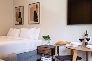 Een hotelkamer met een bed, een nachtkastje met lade, een kleine tafel met stoel, en twee ingelijste abstracte schilderijen aan de muur.