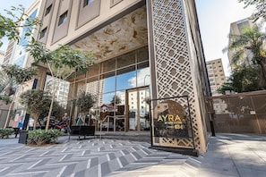 A modern building with a glass facade, a sign for 'AYRA BY GREYSTAR,' and a gated entrance.