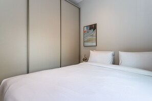 Ein Hotelzimmer mit Bett, Nachttisch, einem Gemälde und einem Kleiderschrank.