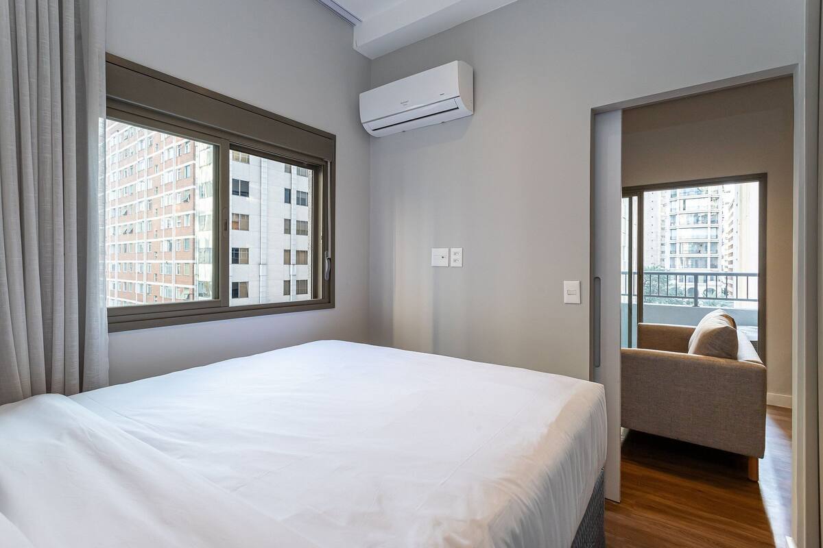 Une chambre d’hôtel avec un lit, une fenêtre, un appareil de climatisation, une chaise et une vue sur le balcon.