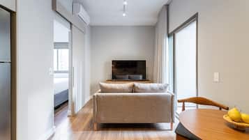 Una sala de estar moderna con un sofá, una mesa de comedor con sillas, un televisor de pantalla plana y un ventanal grande.