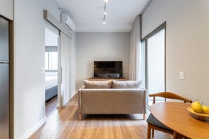 Ein modernes Wohnzimmer mit einer Couch, einem Esstisch mit Stühlen, einem Flachbildfernseher und einem großen Fenster.