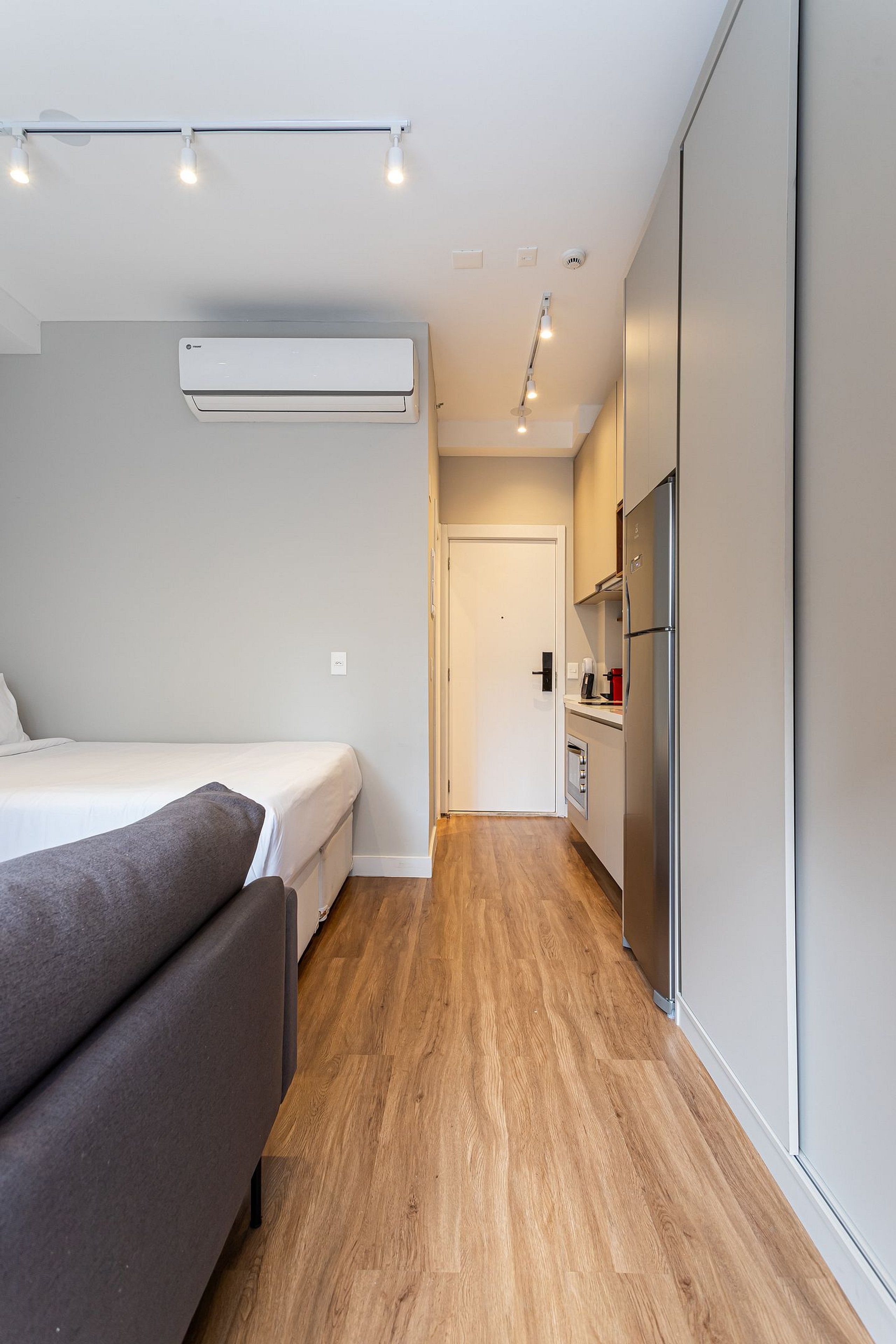 Ein modernes, kompaktes Zimmer mit Bett, Schlafsofa, Küchenzeile und einer Tür zu einem weiteren Raum.