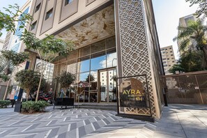 Un edificio moderno con fachada de vidrio, un cartel que indica 'AYRA BY GREYSTAR' y una entrada con puerta de rejas.