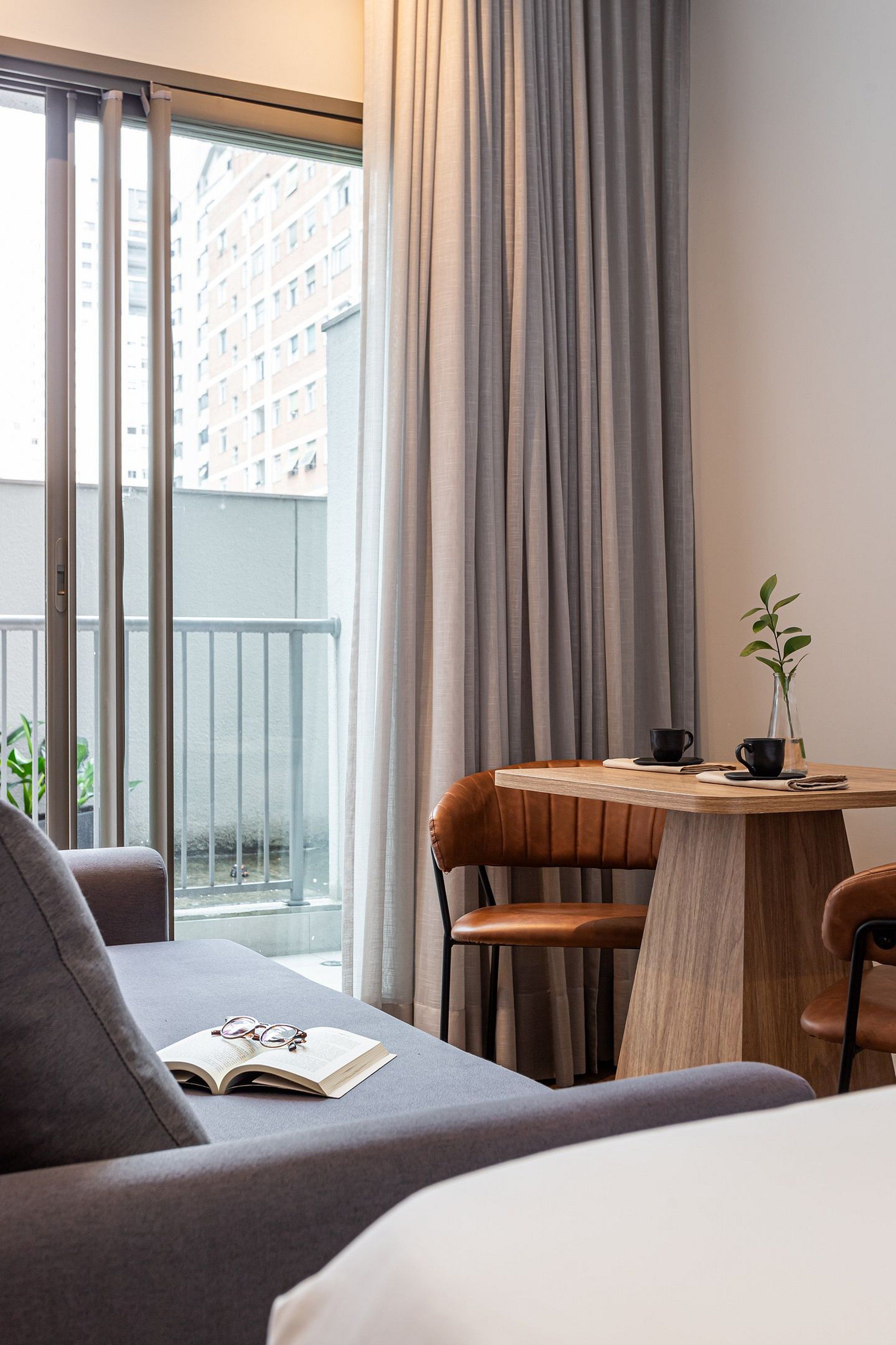A modern hotel room with a balcony, a wooden table, and a sofa.