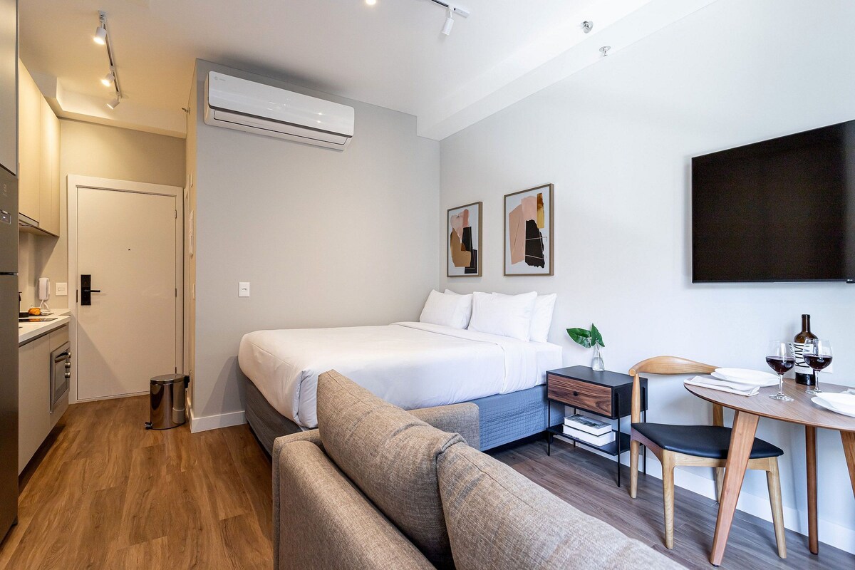 Habitación de hotel con cama, una mesita con una silla, un sofá, un televisor y un aire acondicionado instalado en la pared.
