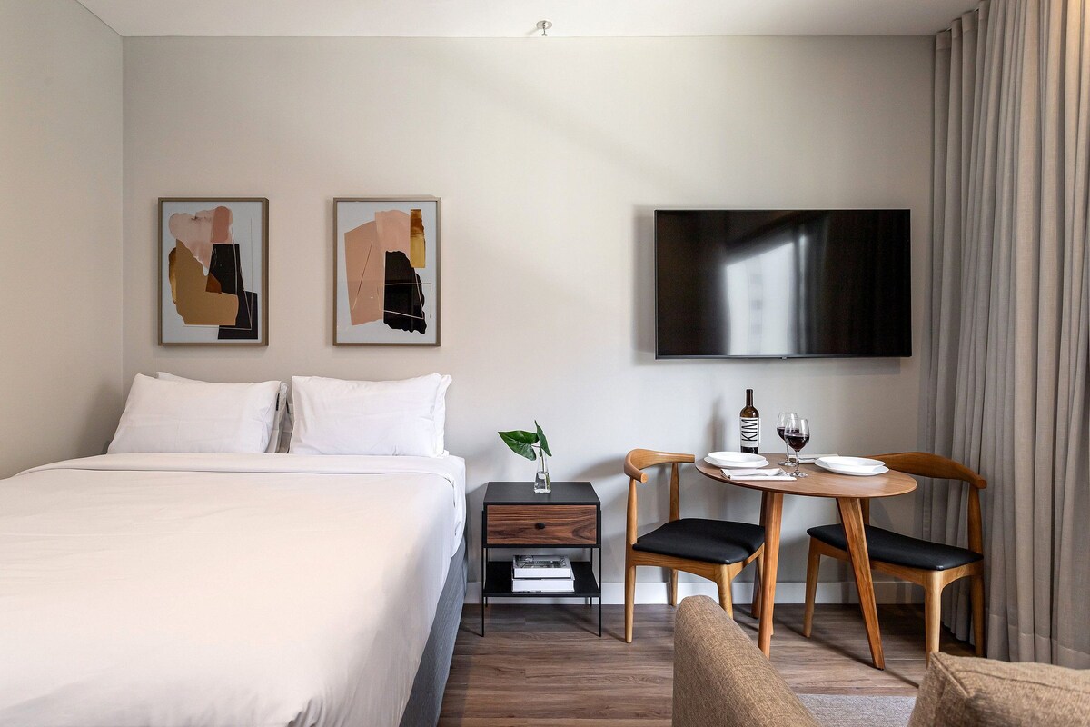 Une chambre d’hôtel comprenant un lit, une table de chevet, une télévision, une table à manger avec des chaises et des œuvres d’art accrochées au mur.