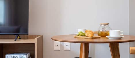 A modern room with a flat-screen TV, a wooden table with chairs, and a shelf with books.