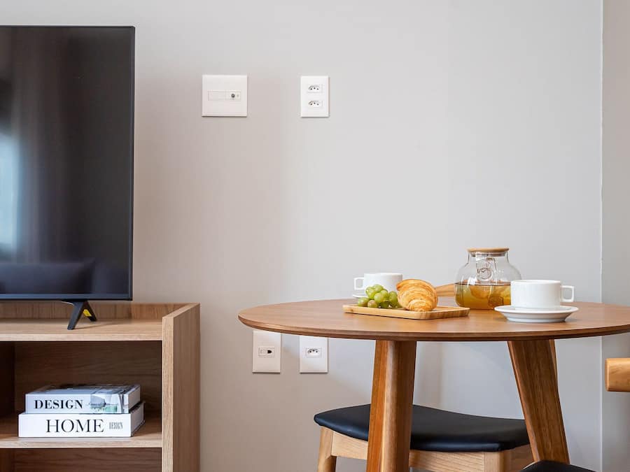 Quarto moderno com televisão de tela plana, uma mesa de madeira com cadeiras e uma estante com livros.