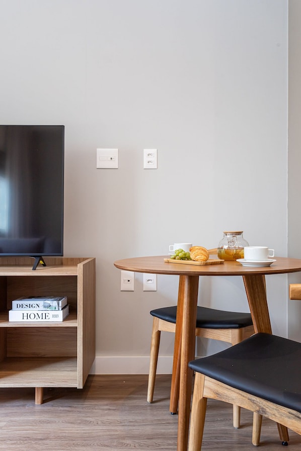 Una habitación moderna con una televisión de pantalla plana, una mesa de madera con sillas y una estantería con libros.