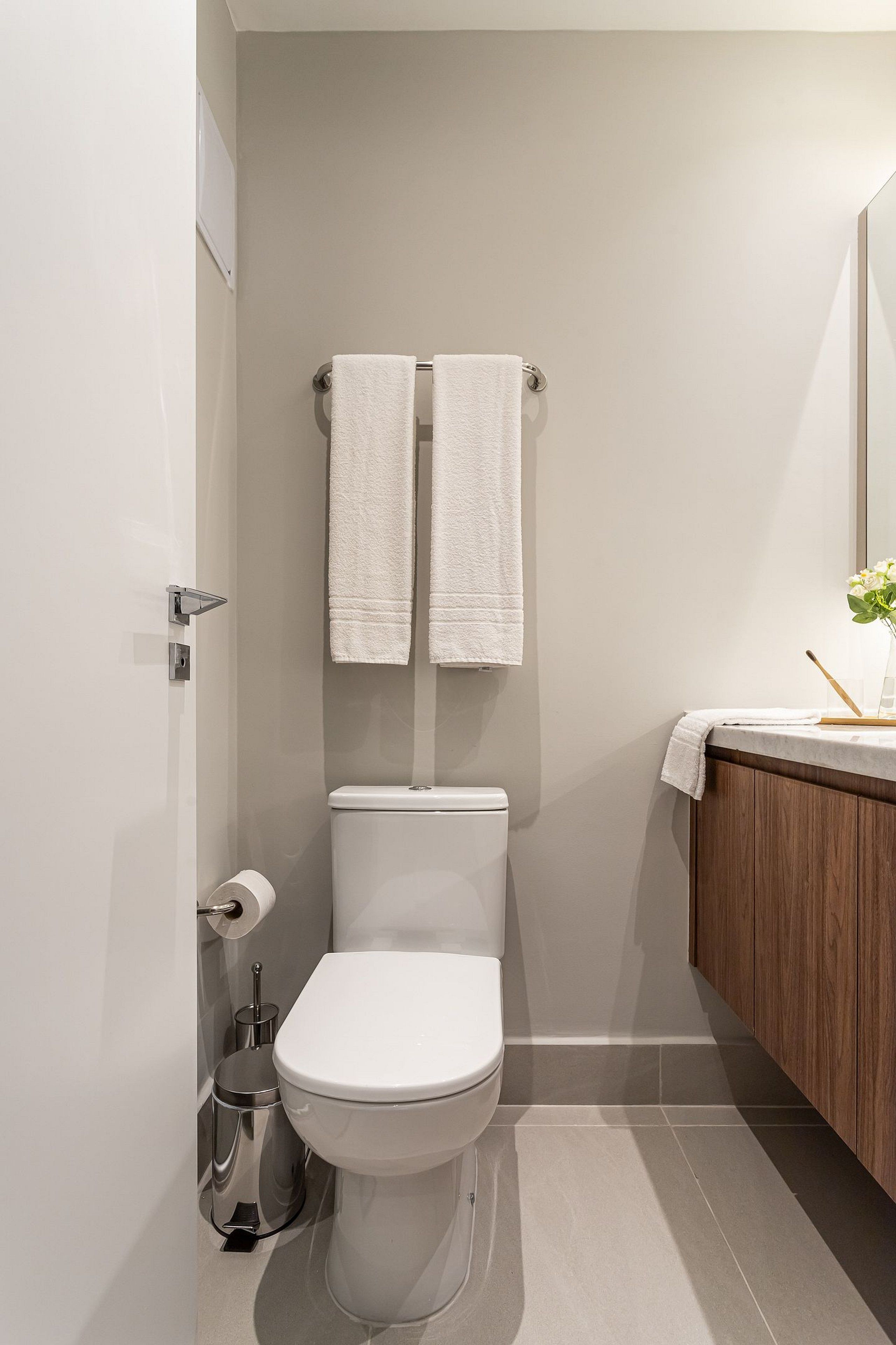A modern bathroom with a toilet, a bidet, a towel rack with two towels, a wooden vanity, and a mirror.